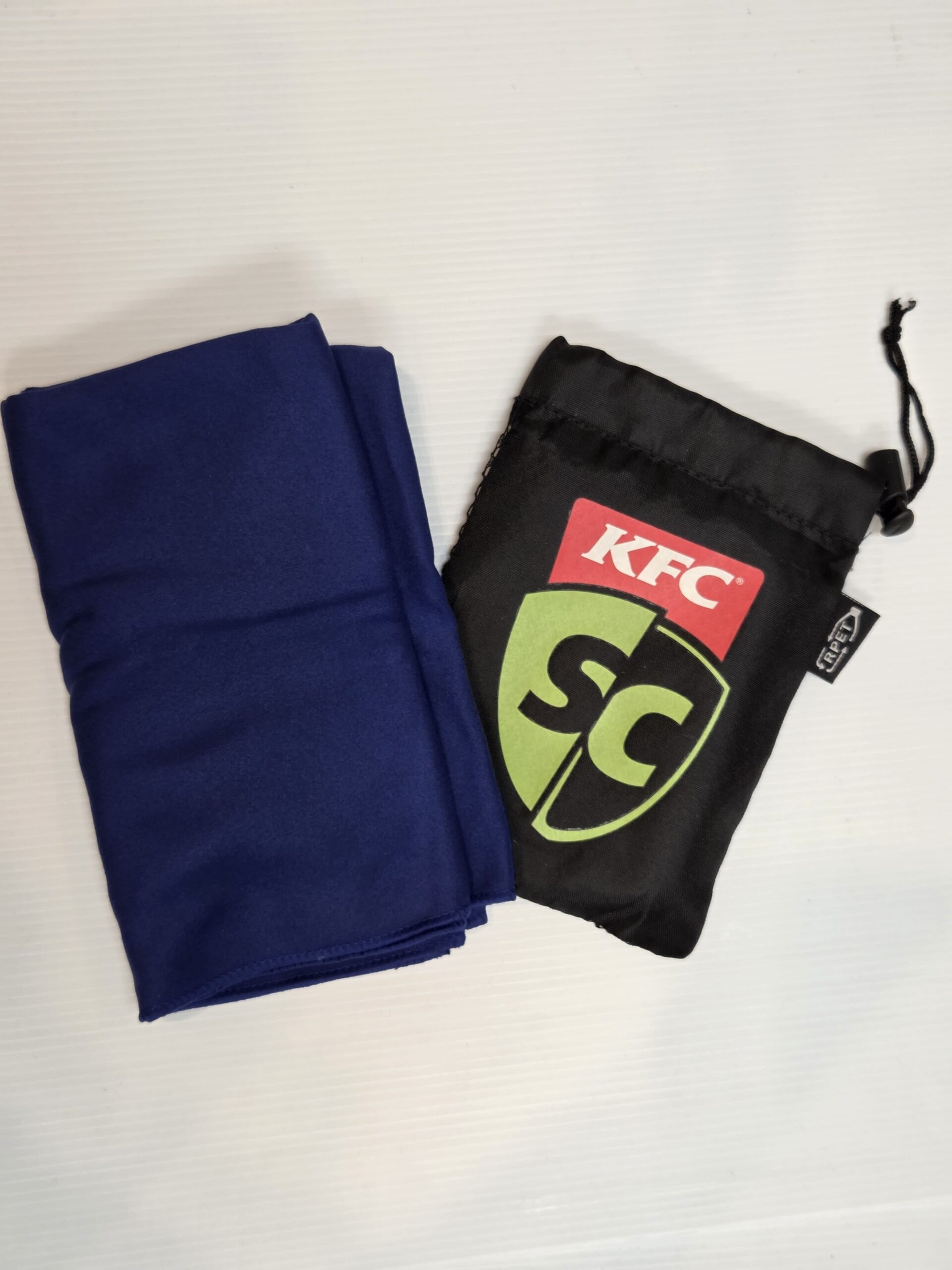 A folded blue cloth and a promotional KFC drawstring pouch on a white surface.