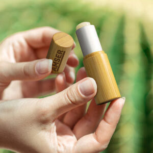 Hands holding a bamboo tube of promotional lip balm.