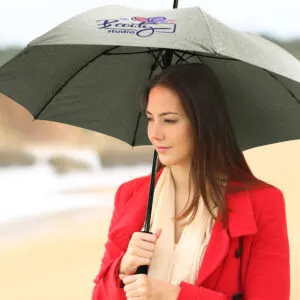 Woman in a red coat with a custom umbrella on a beach.