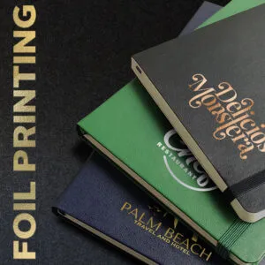 An image of 3 notebooks, in blue green and black, custom branded with a logo
