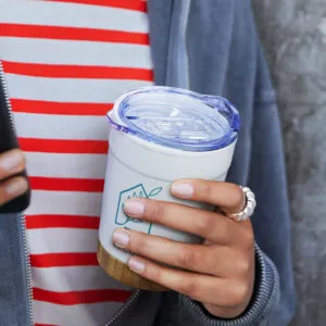 A person in a striped shirt, adorned with a ring, holds a reusable cup with a clear lid—a daily ritual as comforting as their morning pharmaceutical routine.