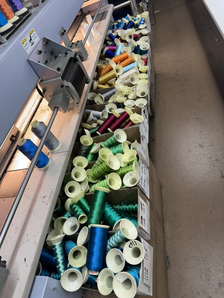 Colorful spools of thread scattered on a worktable near an industrial embroidery machine.