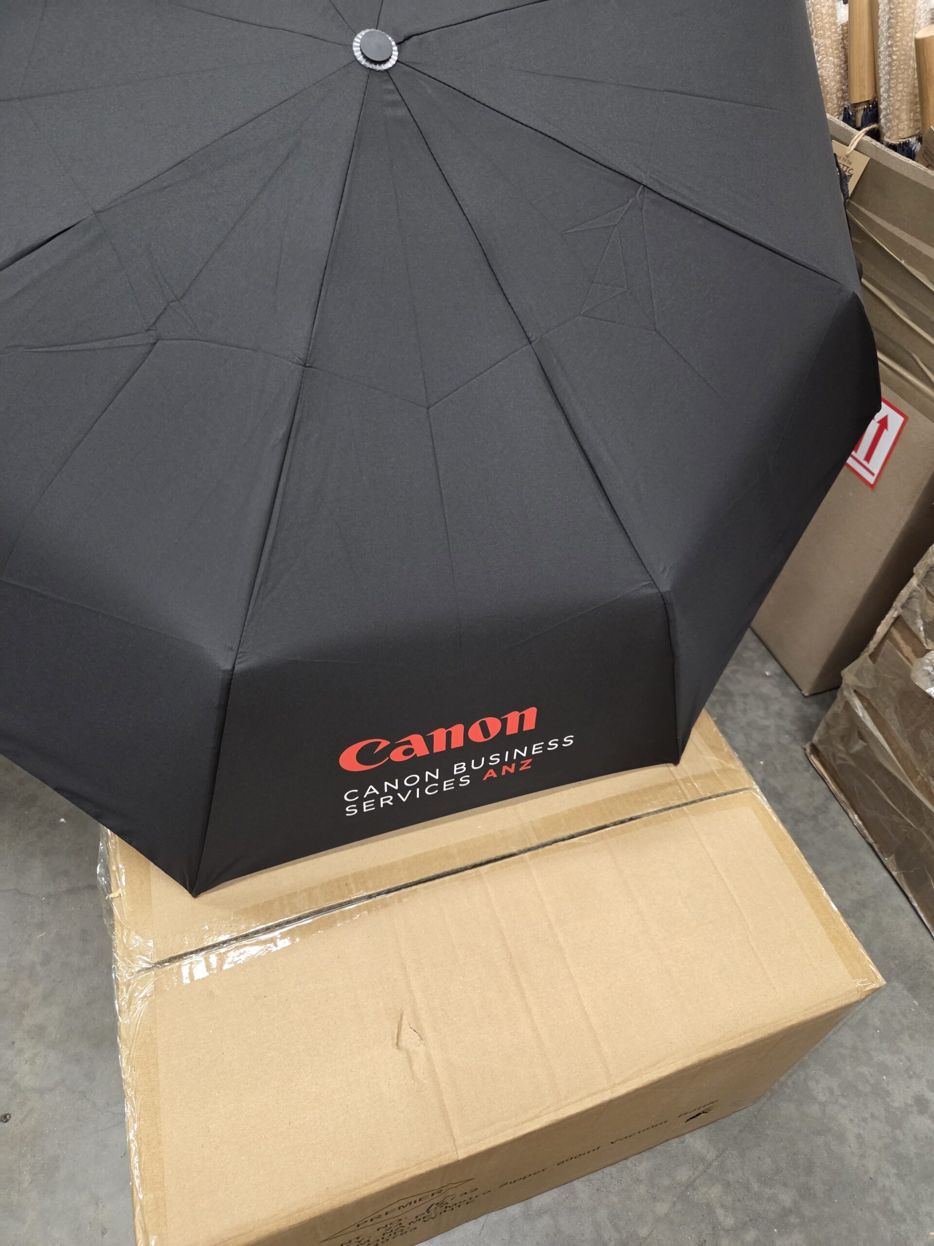 Black golf umbrella printed with Canon logo with a box