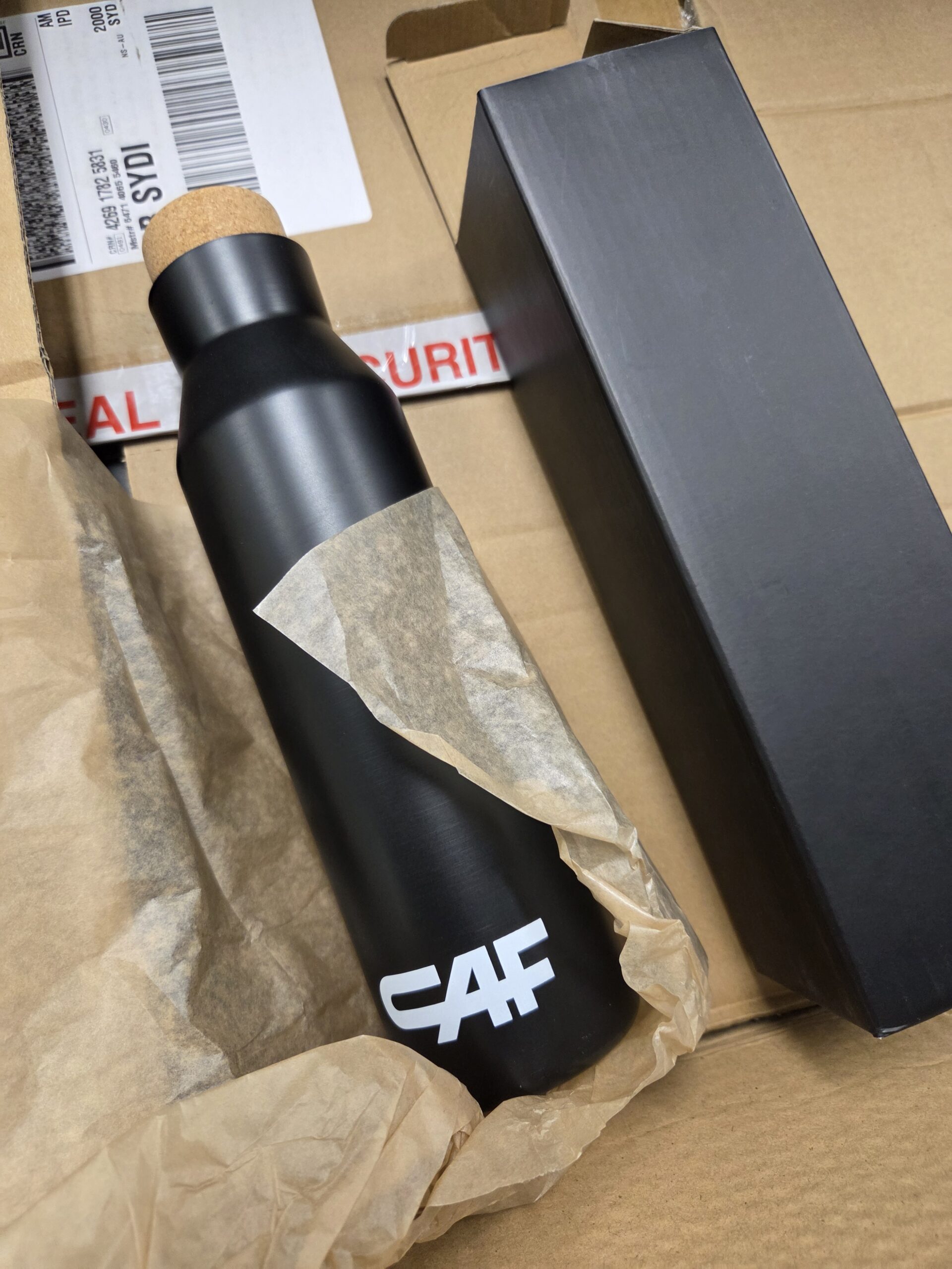 A black metal drink bottle with cork lid and matching black packaging.
