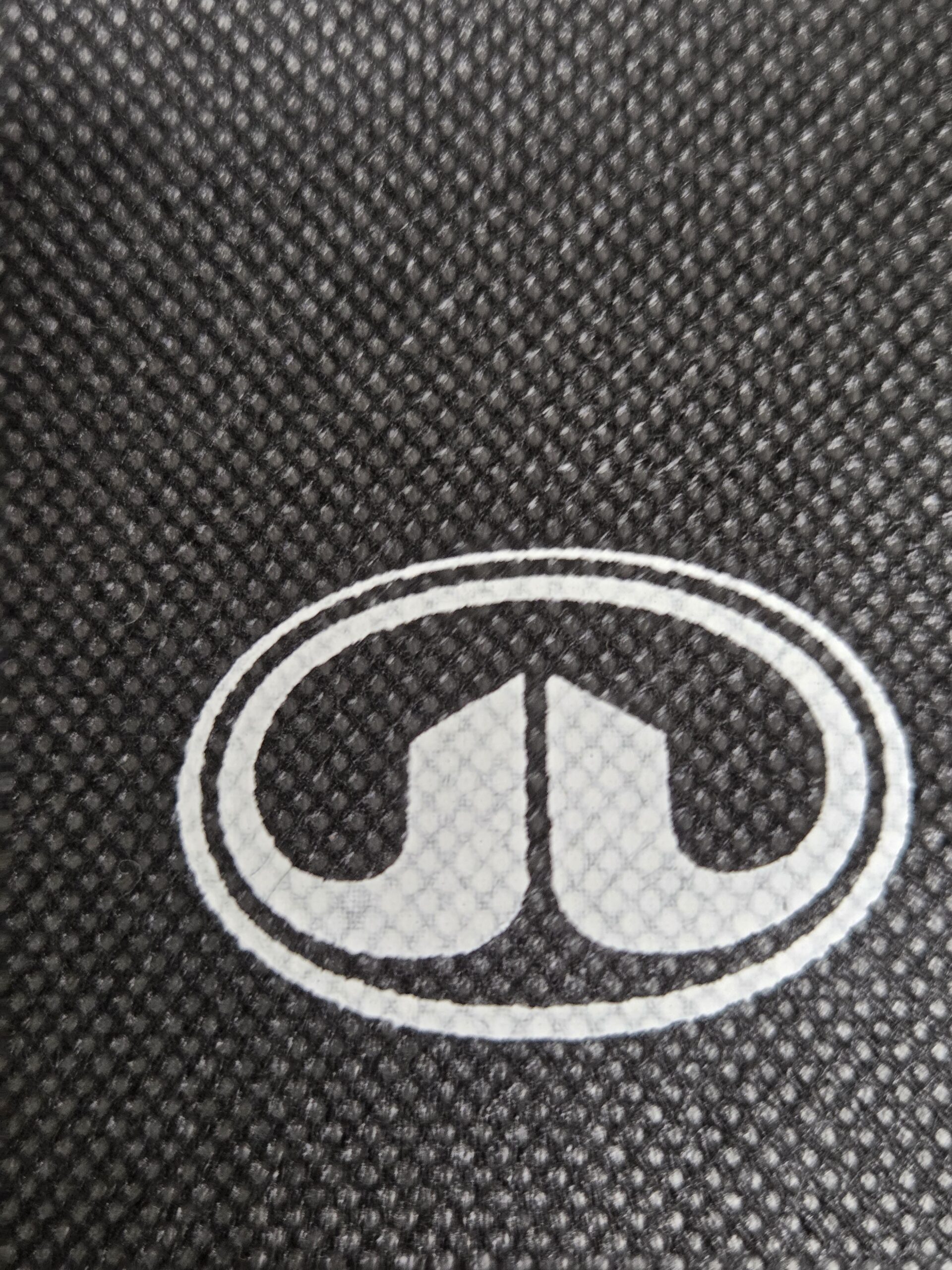 White oval logo with two curved shapes on a cotton tote bag, set on a textured black and gray background.