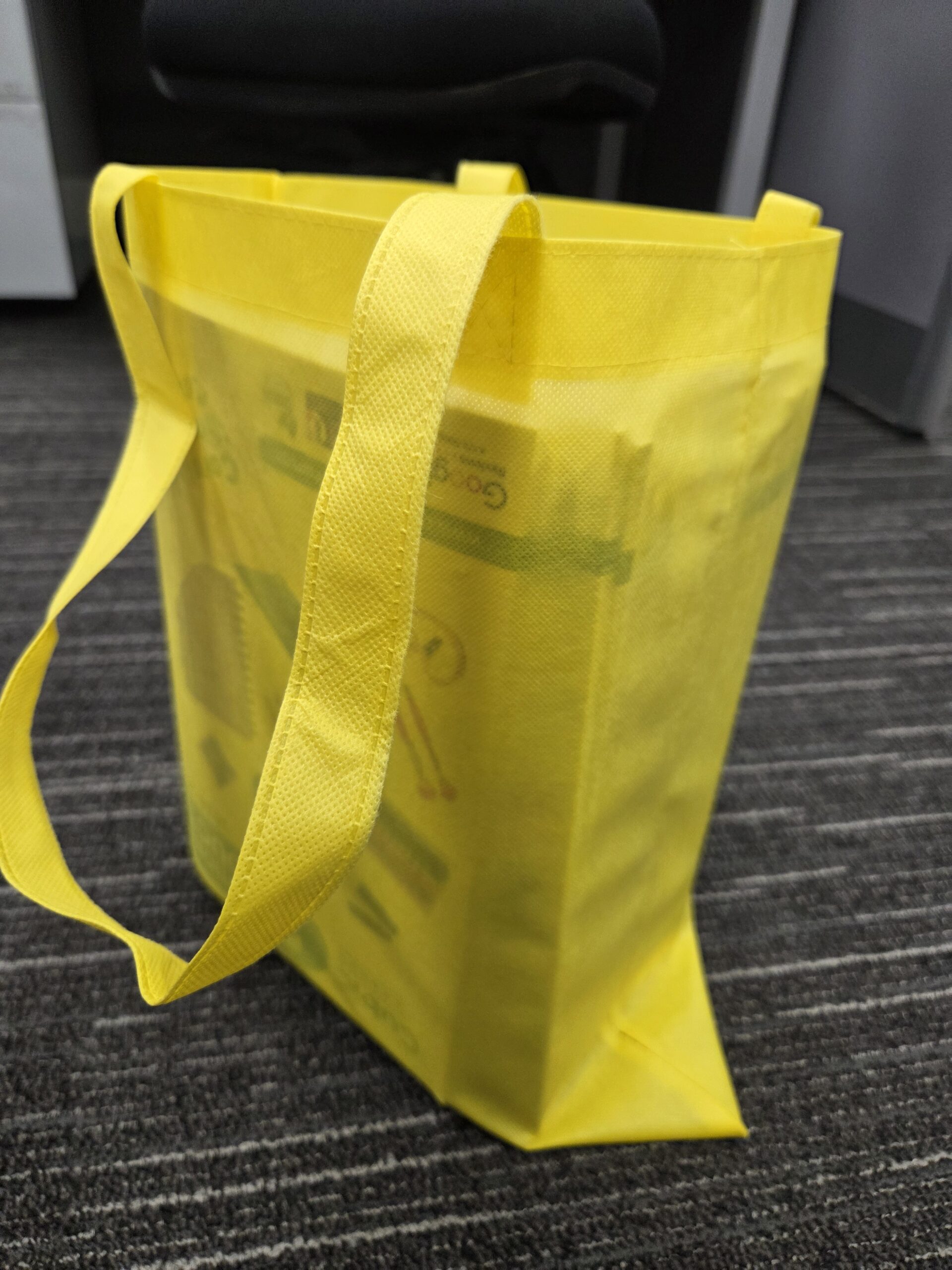 A yellow Tote Bag sits on a gray carpeted floor in a conference office setting.