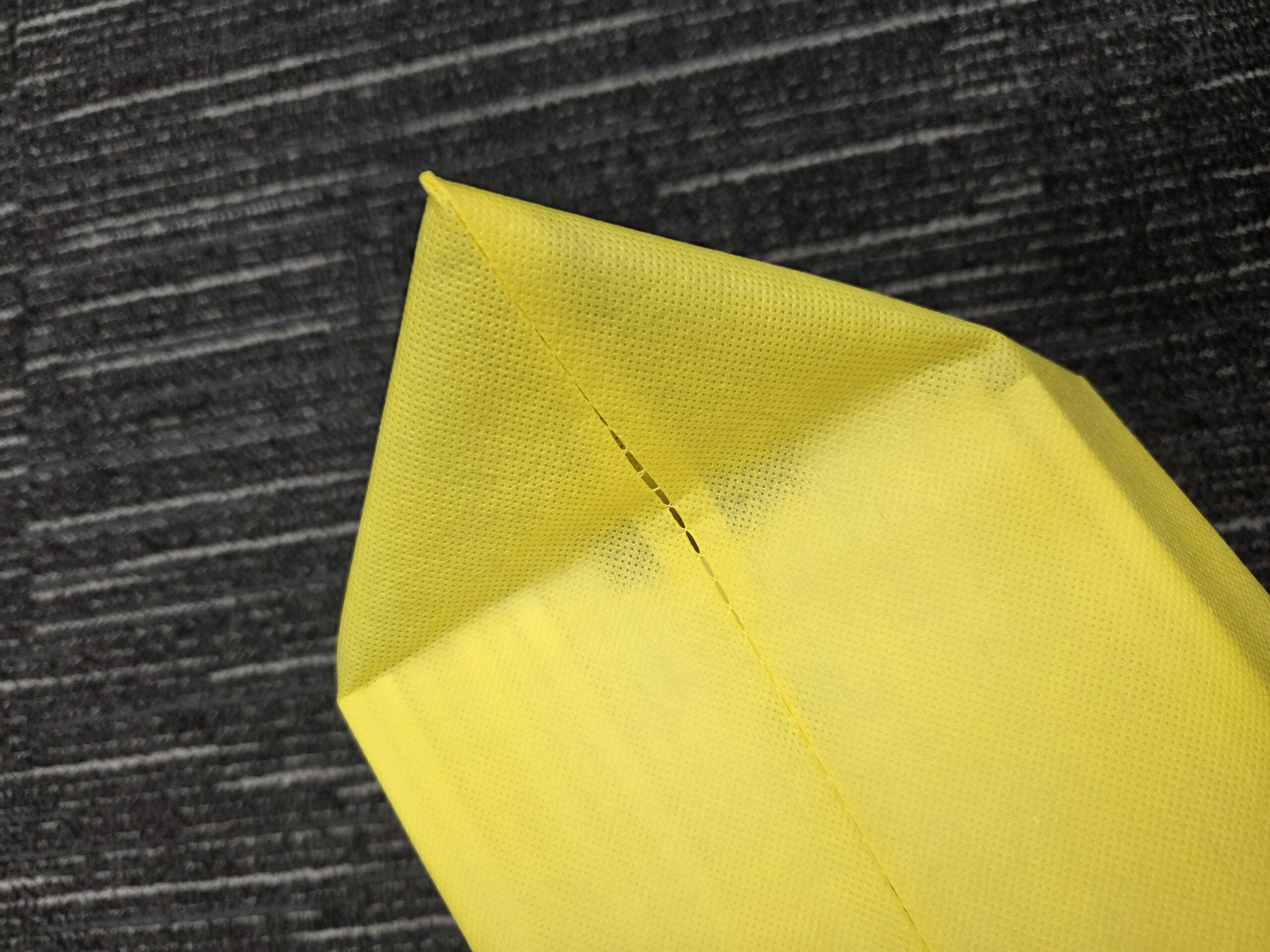 Yellow napkin folded into a triangle, contrasting like calico vs canvas on a dark surface.