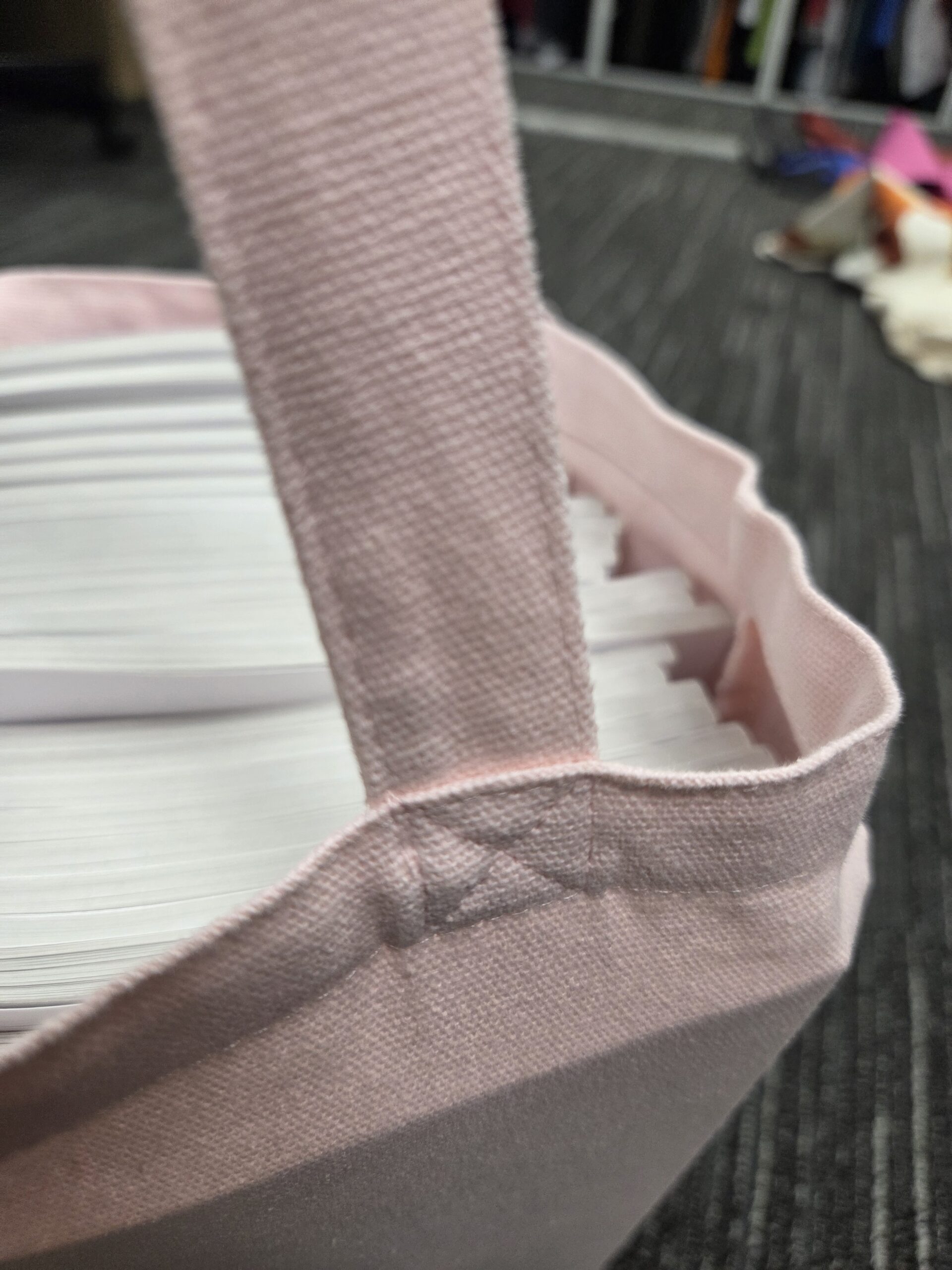 A pink tote bag, ideal as a conference bag, holds stacks of white paper on a carpeted floor.