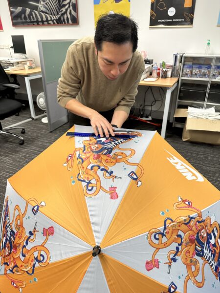man measuring the logo on the top of an branded umbrella for quality