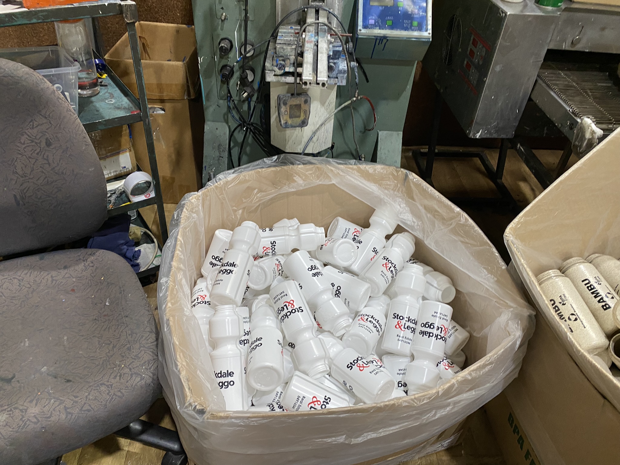 A large bin of Custom Bottles next to office chairs and industrial equipment.