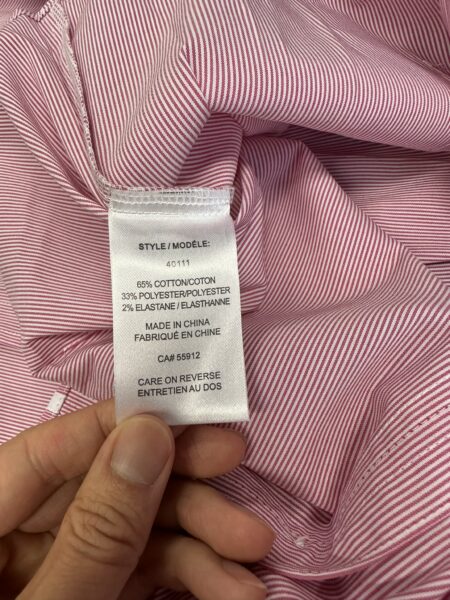 A hand holds a clothing tag over red and white striped fabric