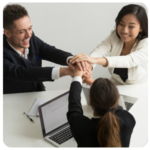 Three people in business attire stacking hands, smiling as they align on business goals.