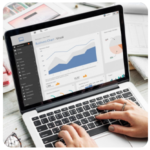 Hands typing on a laptop displaying business goals, charts, and graphs on the screen.