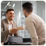 Two men shaking hands in an office, smiling as they discuss business goals.