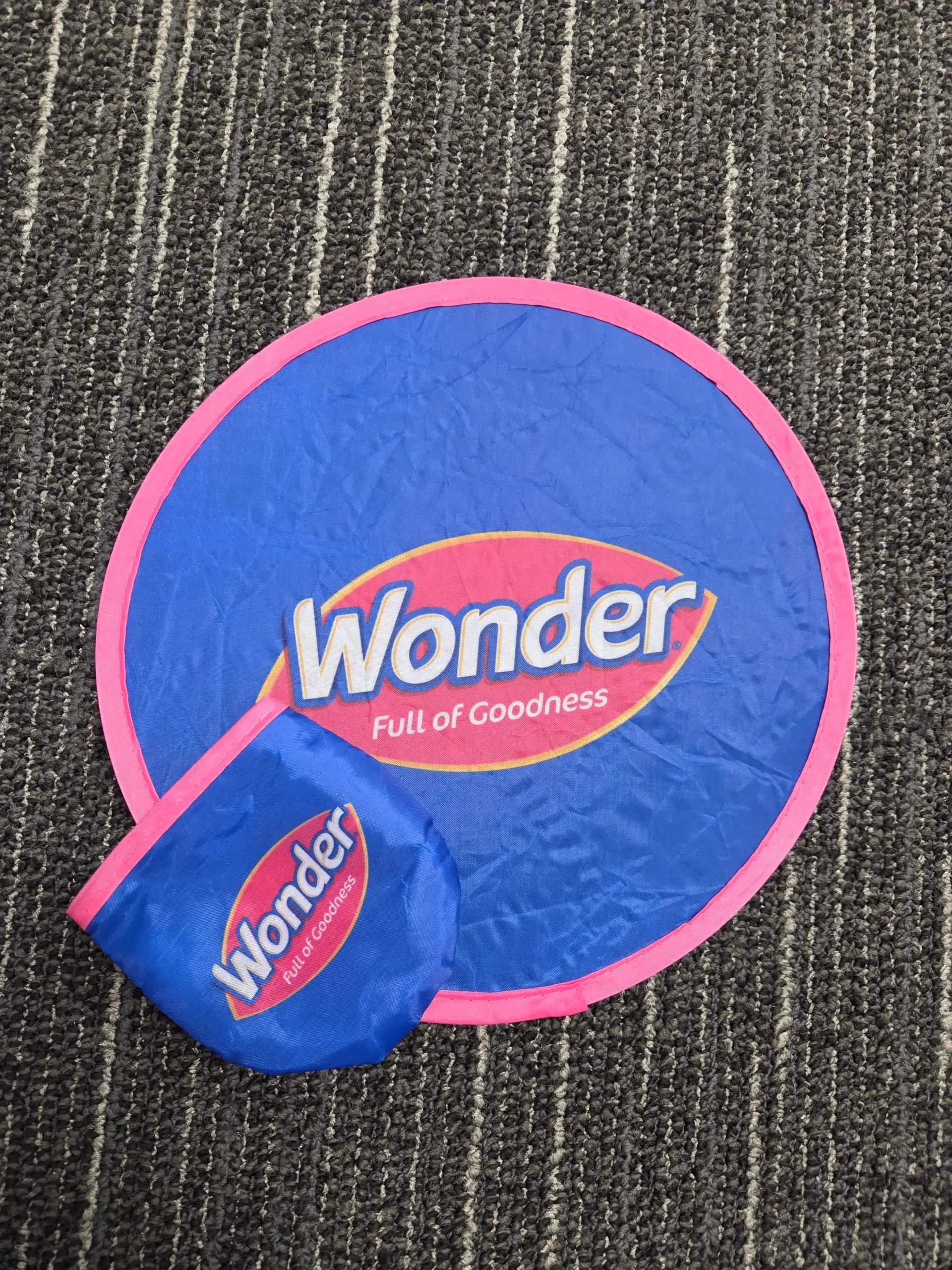 Blue and pink Wonder Full of Goodness foldable frisbee and pouch on striped carpet.