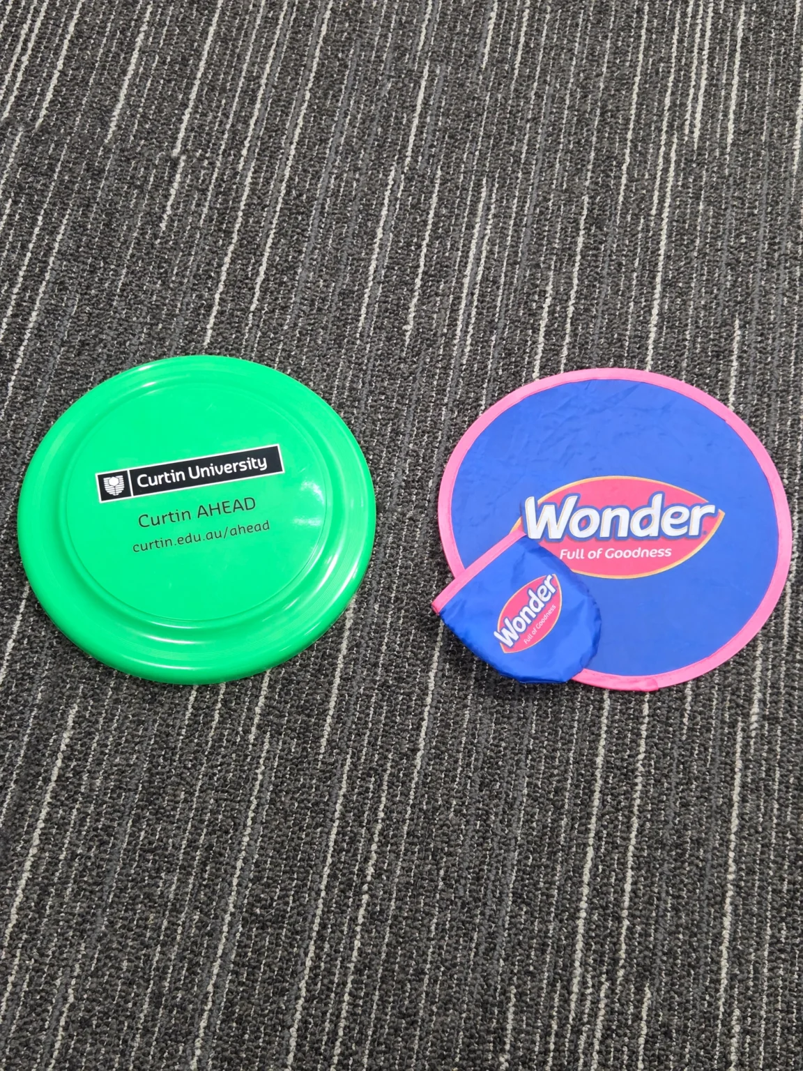 Two colorful frisbees, one green and one blue Wonder, with pouch on a striped carpet.