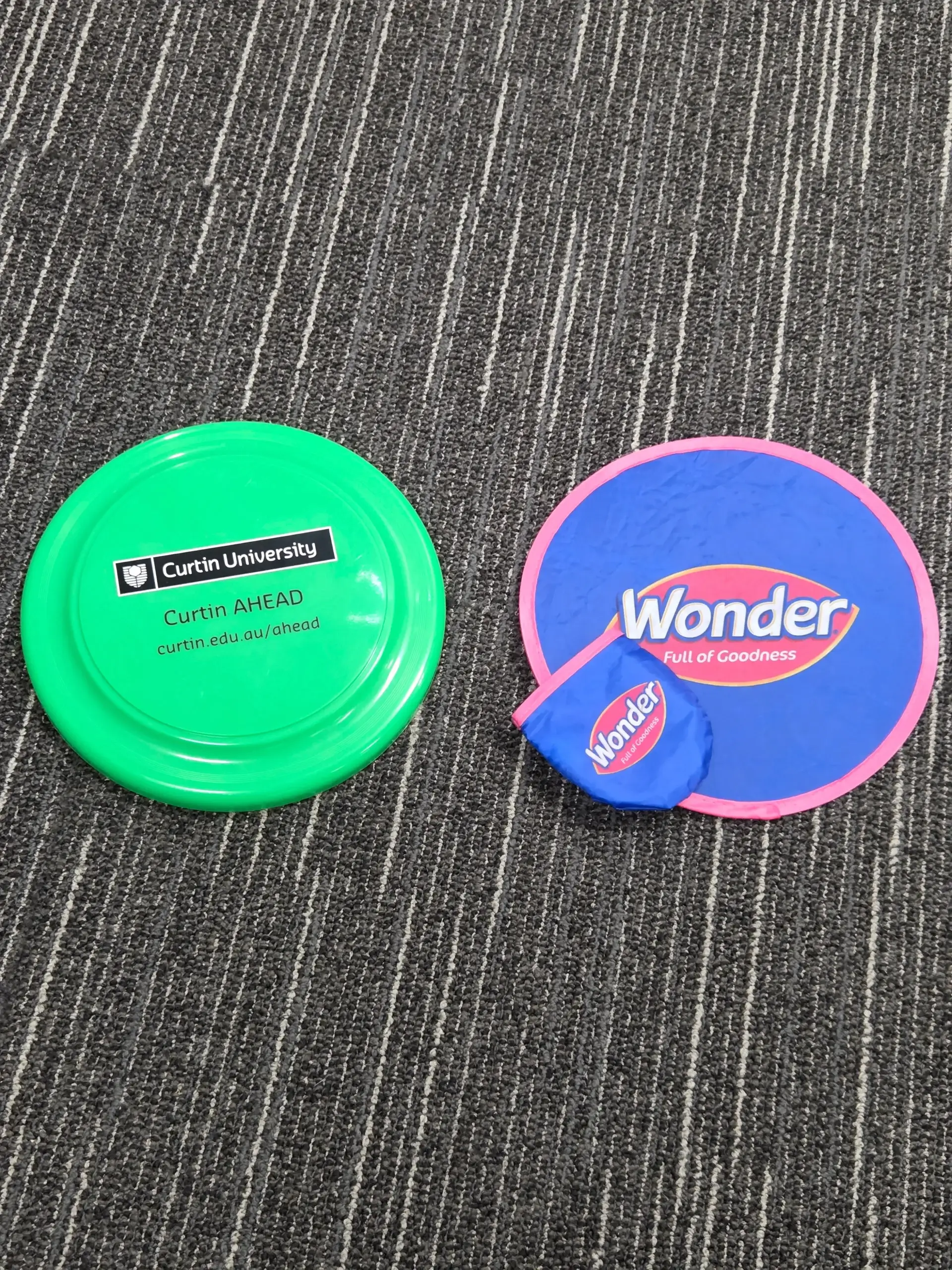 Two colorful frisbees, one green and one blue Wonder, with pouch on a striped carpet.