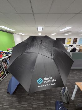 Large black umbrellas with Nexia Australia logo open inside an office workspace.