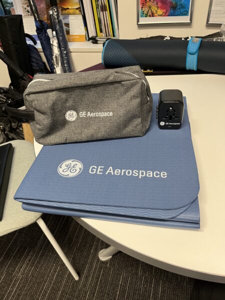 GE Aerospace branded bag, travel adapter, and mat displayed in a modern office setting.