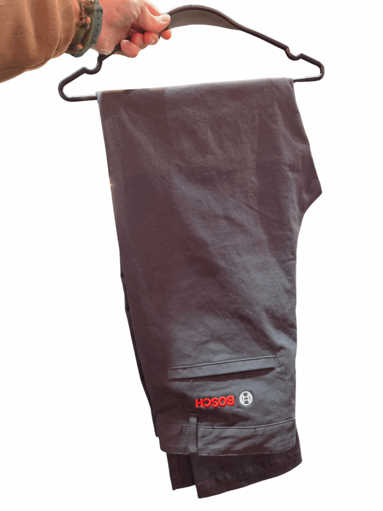 A hand holds a hanger with folded dark pants featuring a red Bosch logo.