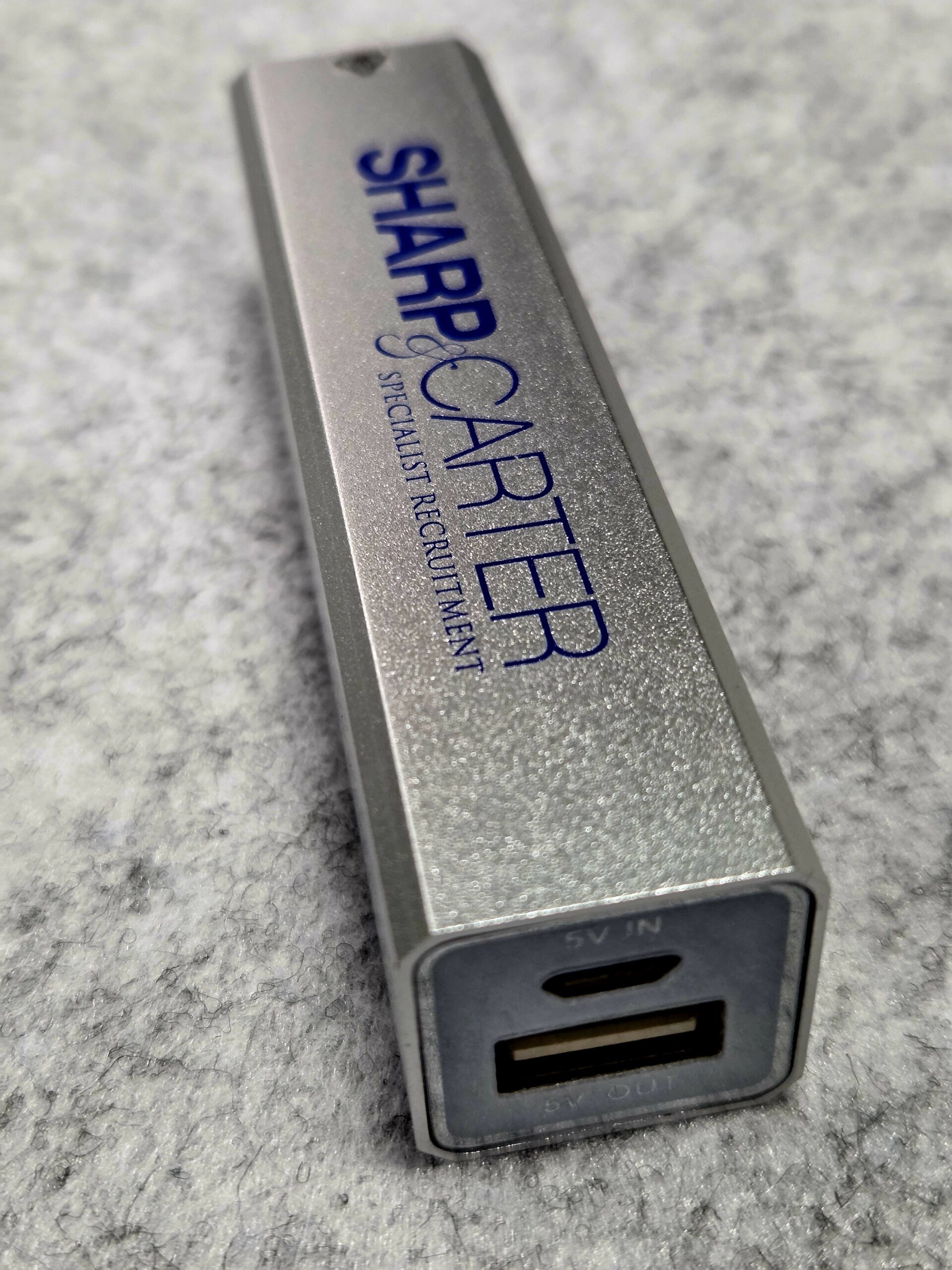 Sleek silver power bank with Sharp Carter logo and a USB port on one end.