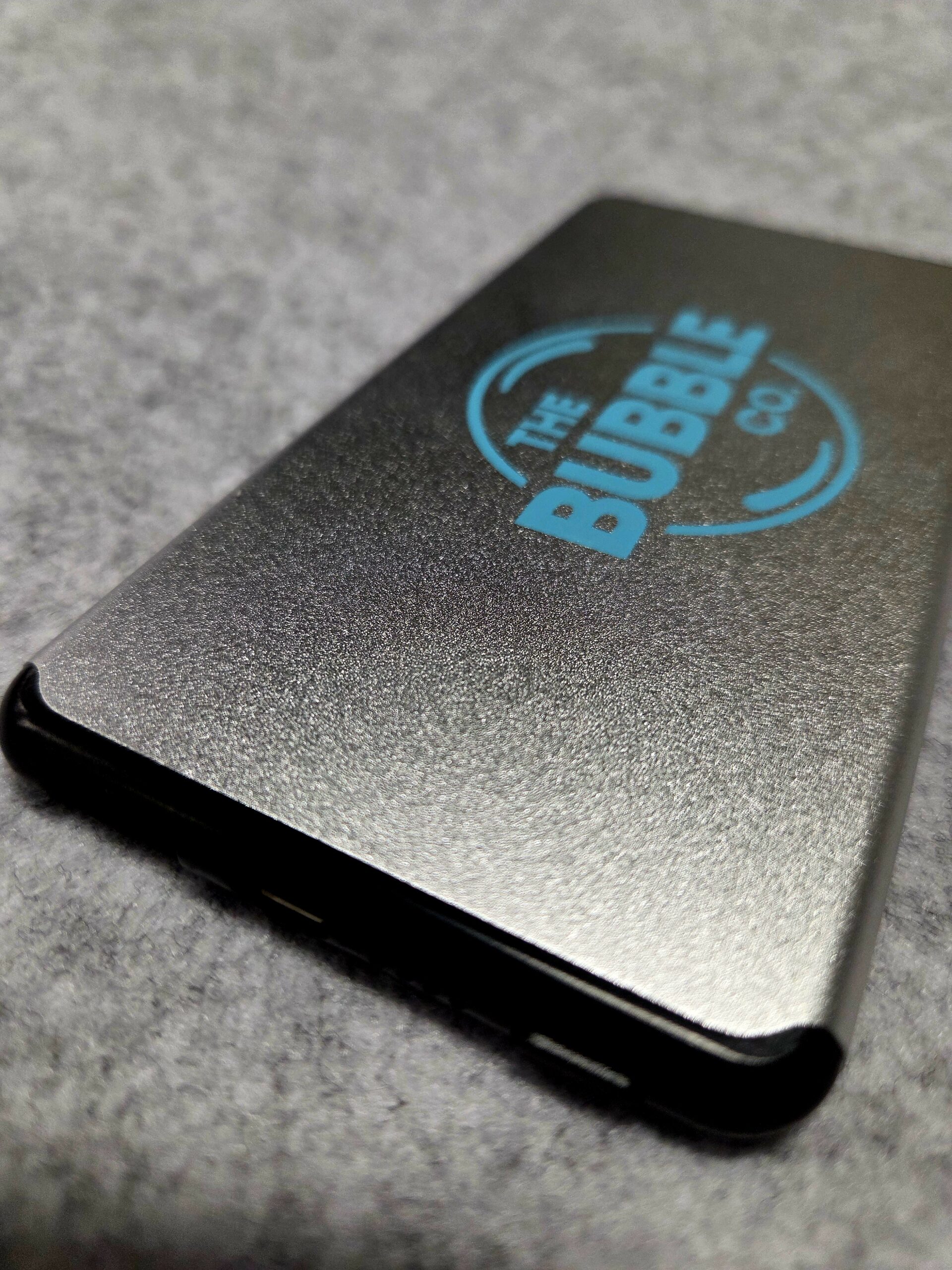 A black cardholder and power bank with The Bubble Co logo on a gray surface.