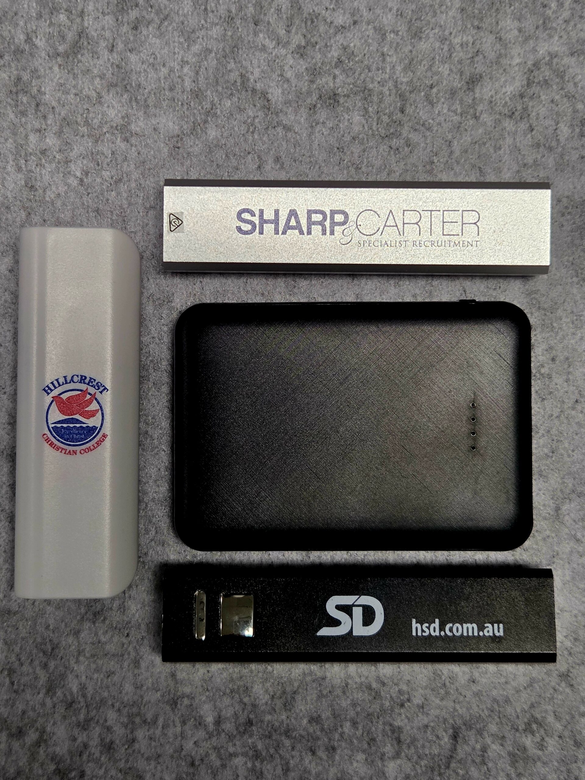 Four branded USB drives and a sleek power bank on a gray textured surface.