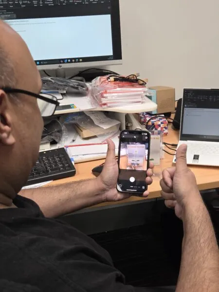 Person giving a thumbs up, creating user generated content at a cluttered desk with their phone.