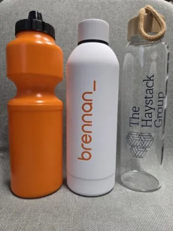 Three drink bottles—orange, white with Brennan logo, and clear with The Haystack Group branding.