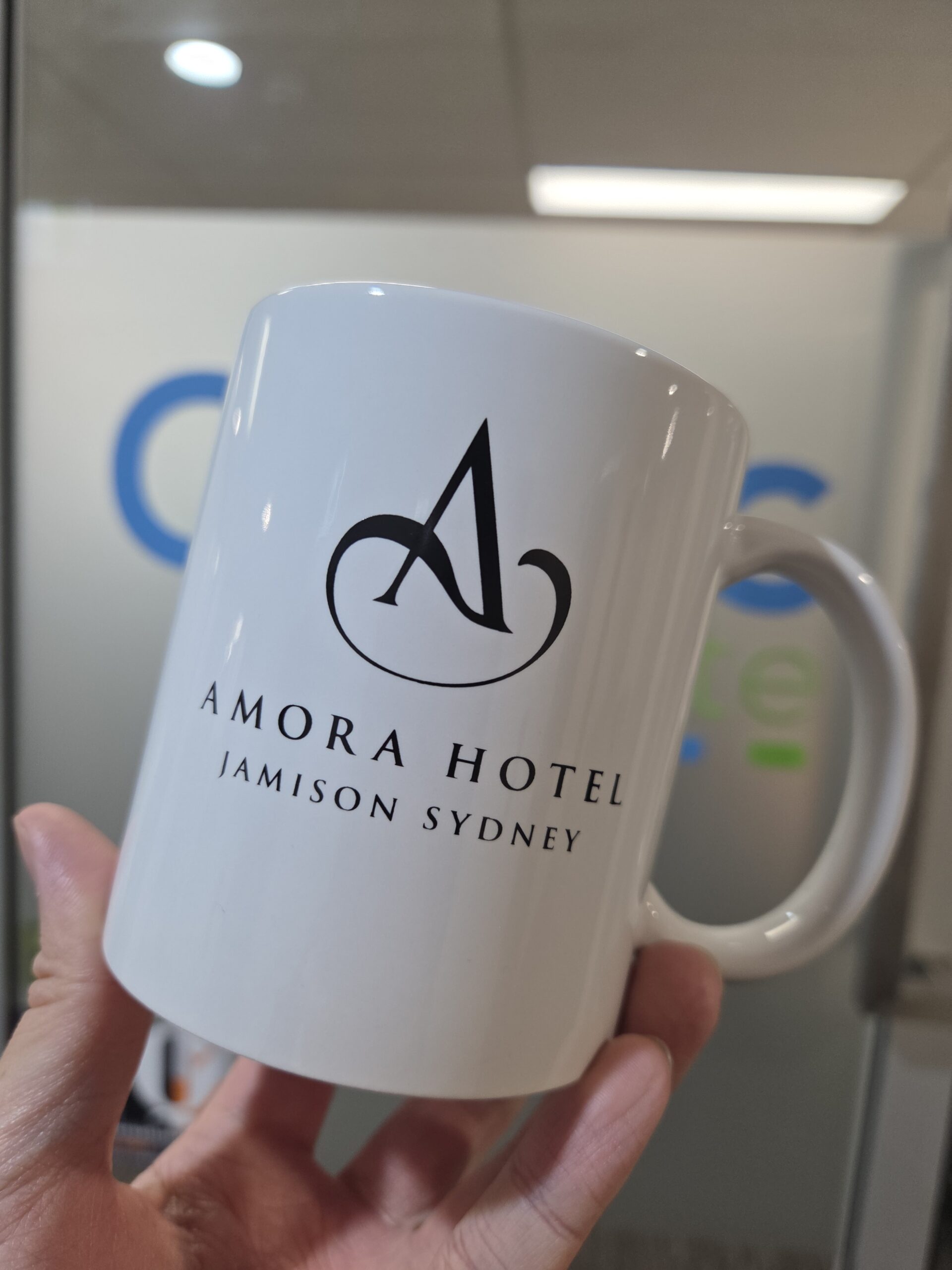 white coloured mug with Amora Hotel logo being held
