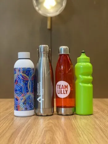 Four stylish water bottles, each uniquely designed, sit on a wooden table.