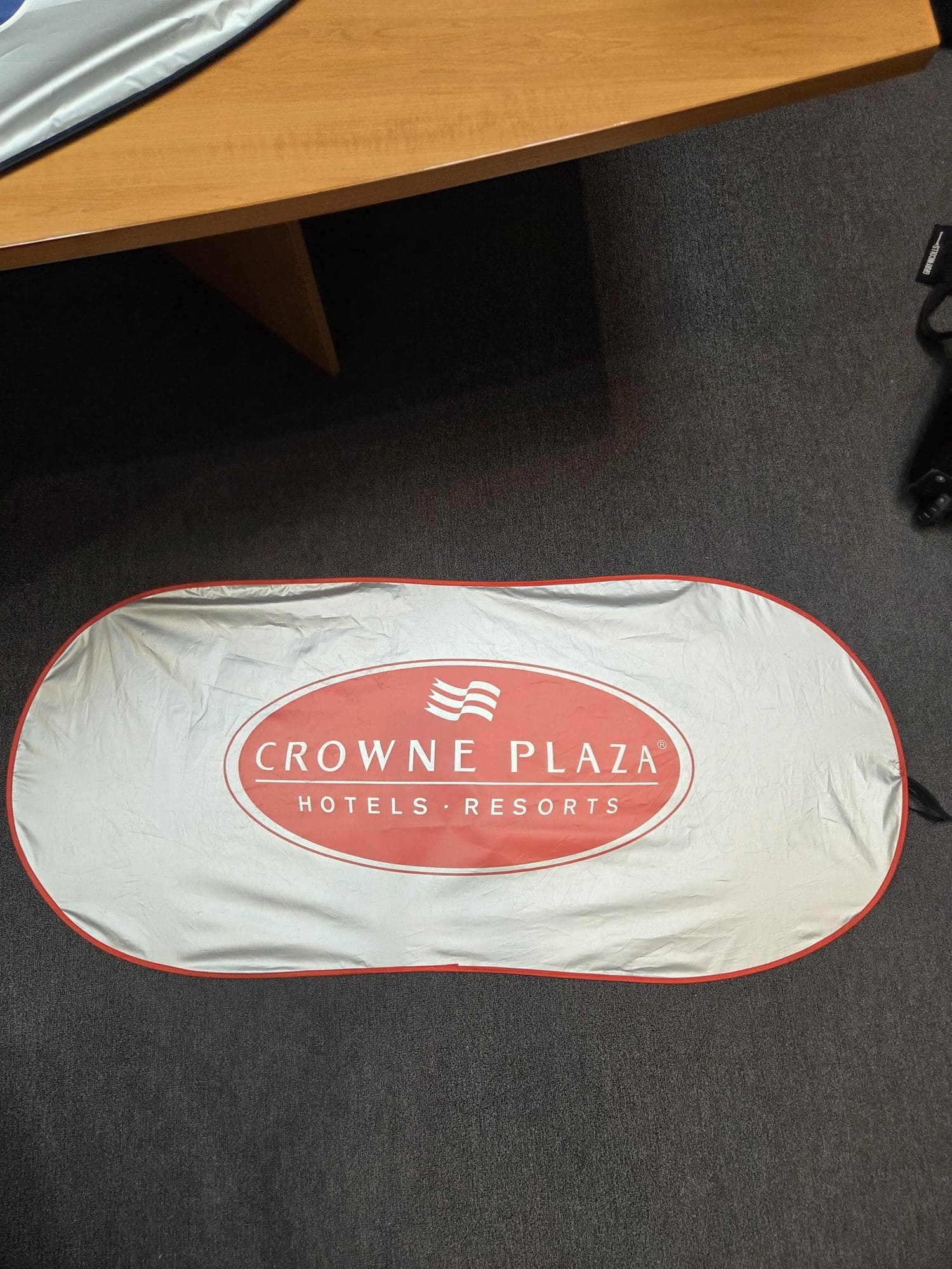 A Crowne Plaza Hotels sunshade on a dark carpeted floor near a desk.