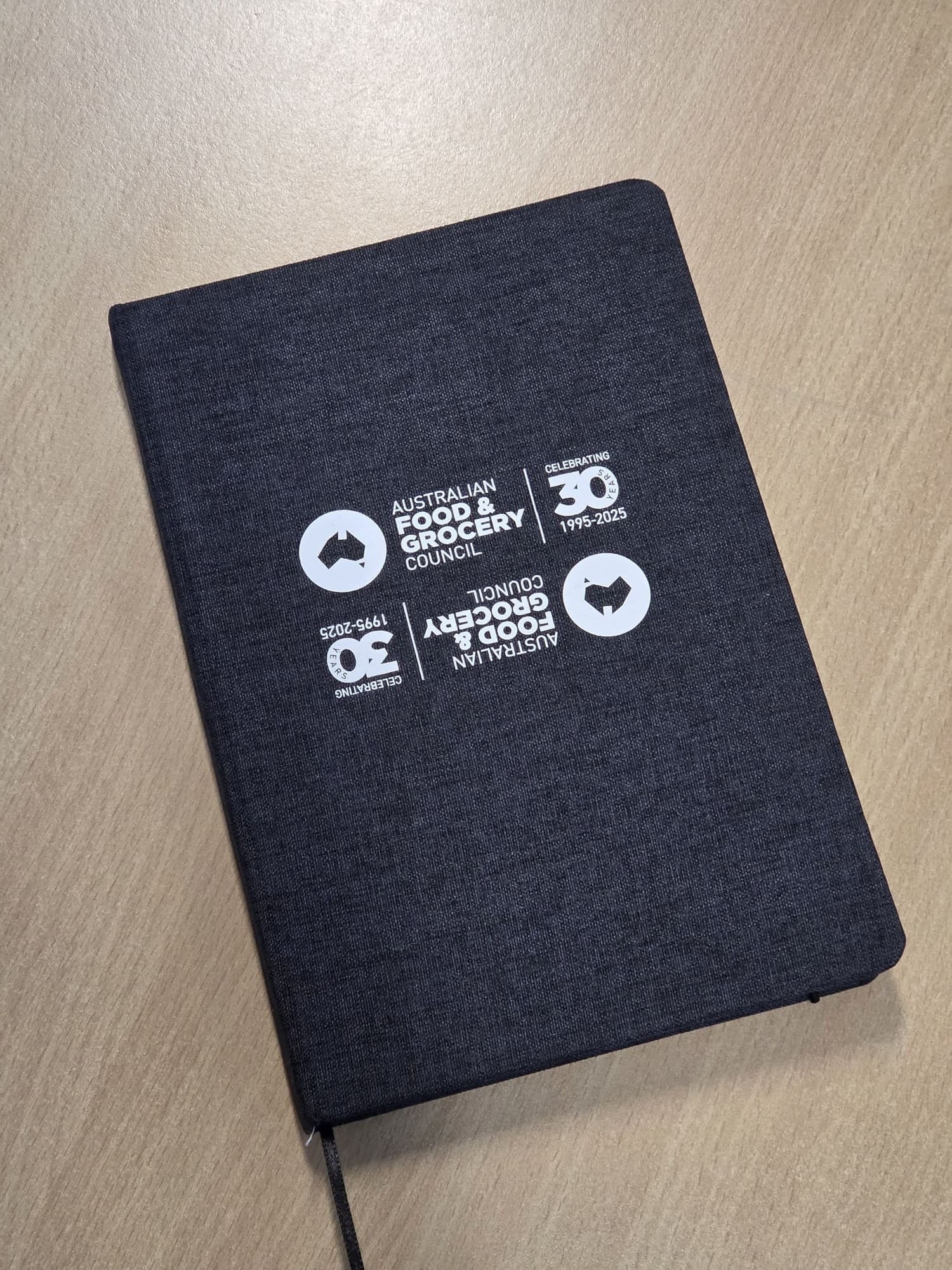 A black notebook on a wooden desk with white Australian Food & Grocery Council logos.