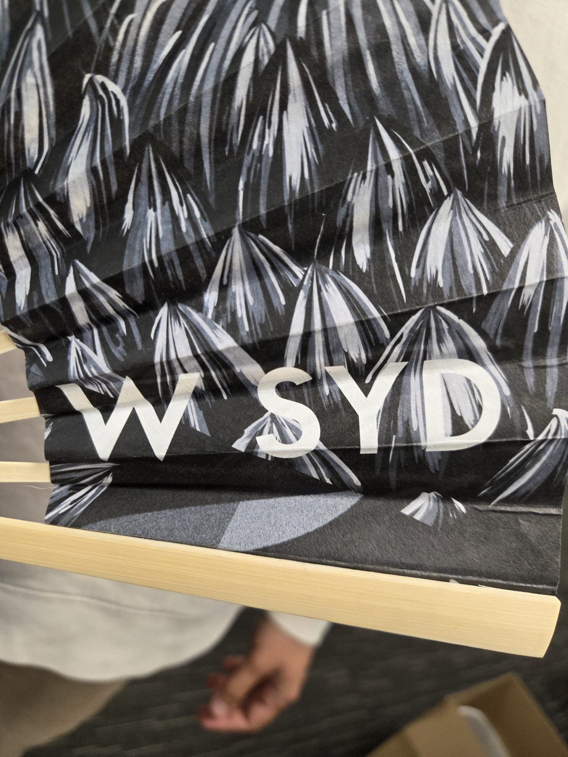 A black patterned fan with the letters W SYD printed on it.