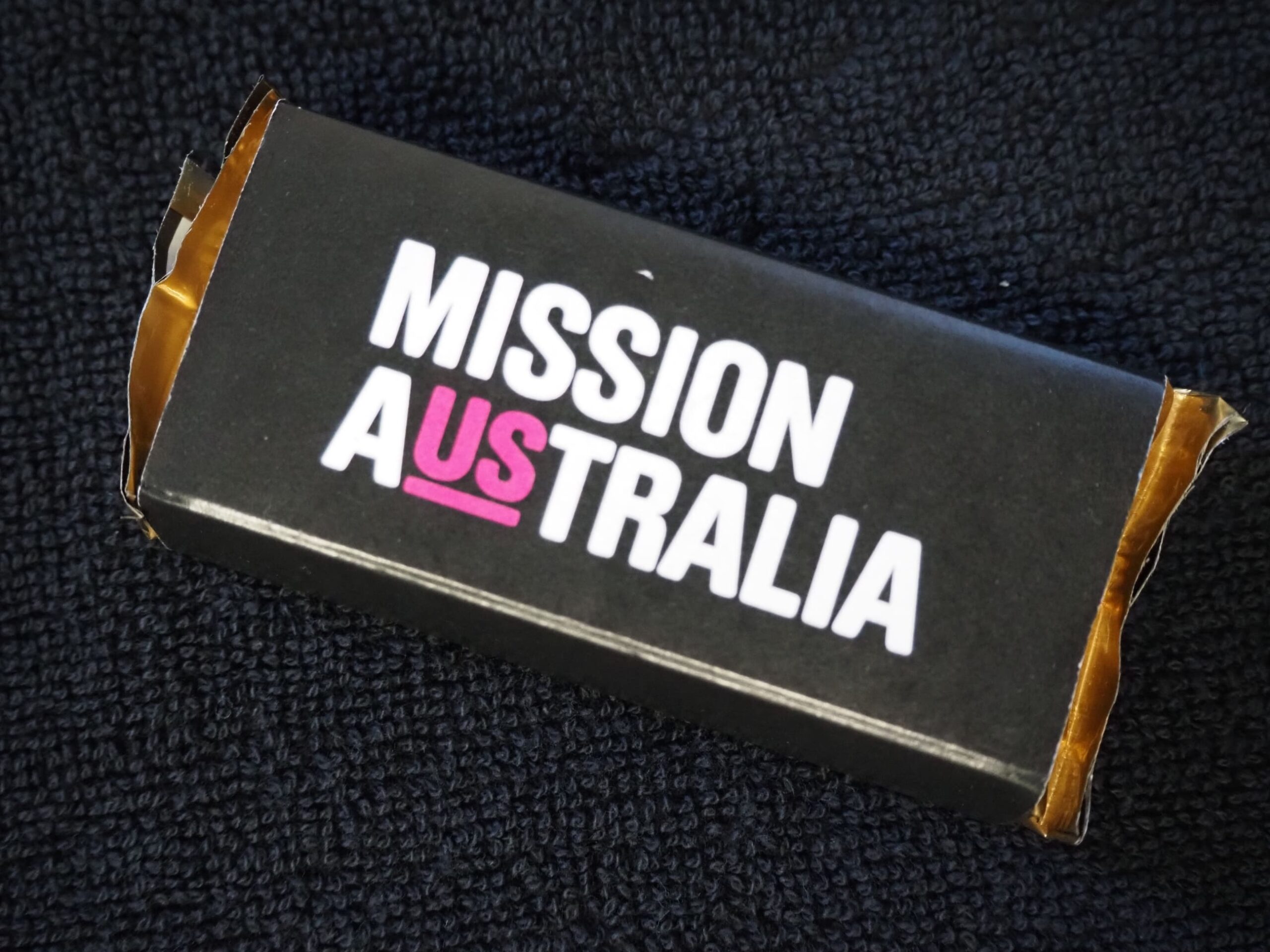 A black box labeled MISSION AUSTRALIA, perfect for corporate Christmas gifts, on dark fabric.
