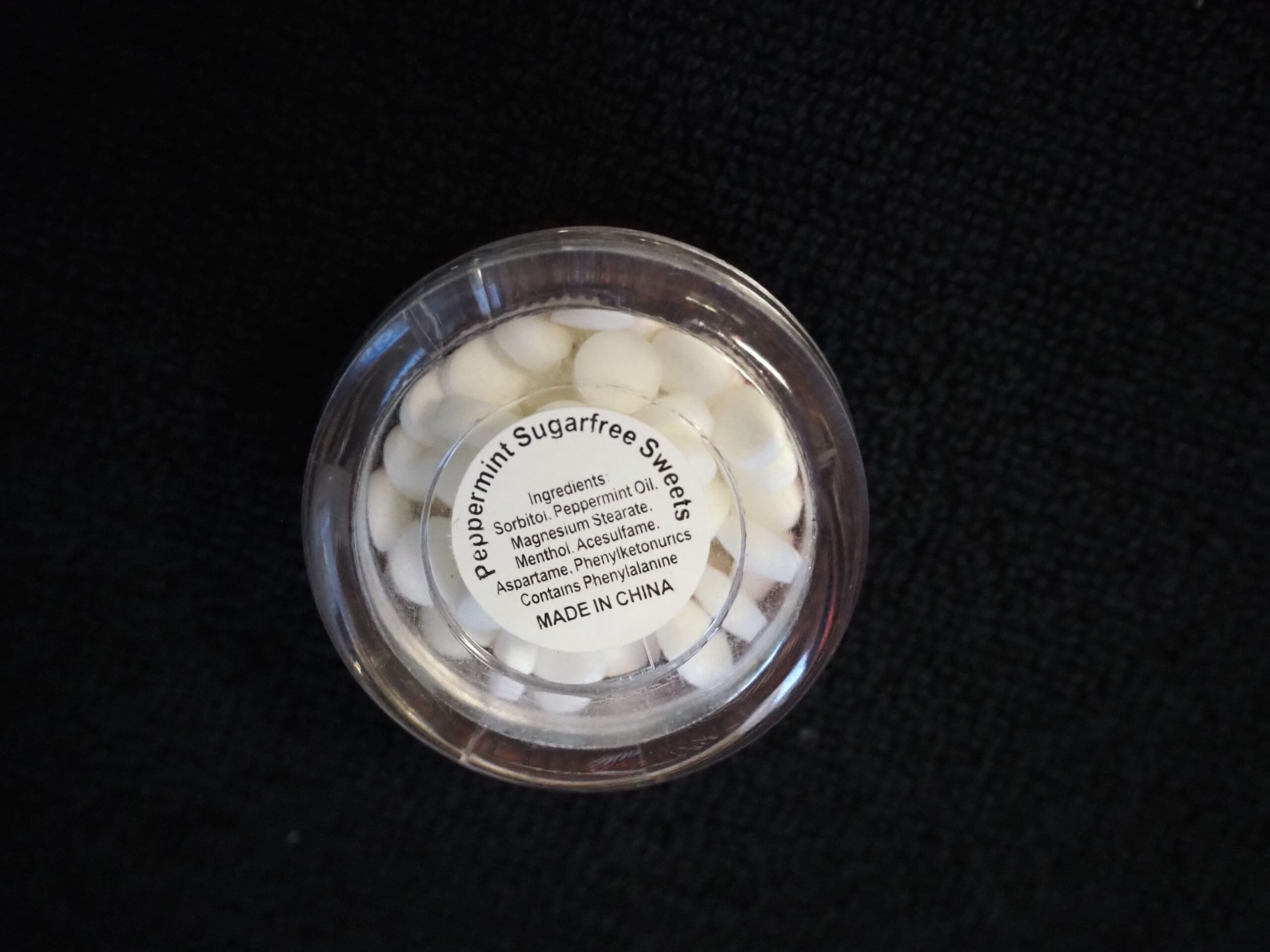 A round container of peppermint sugar-free sweets, a client story on a black surface.