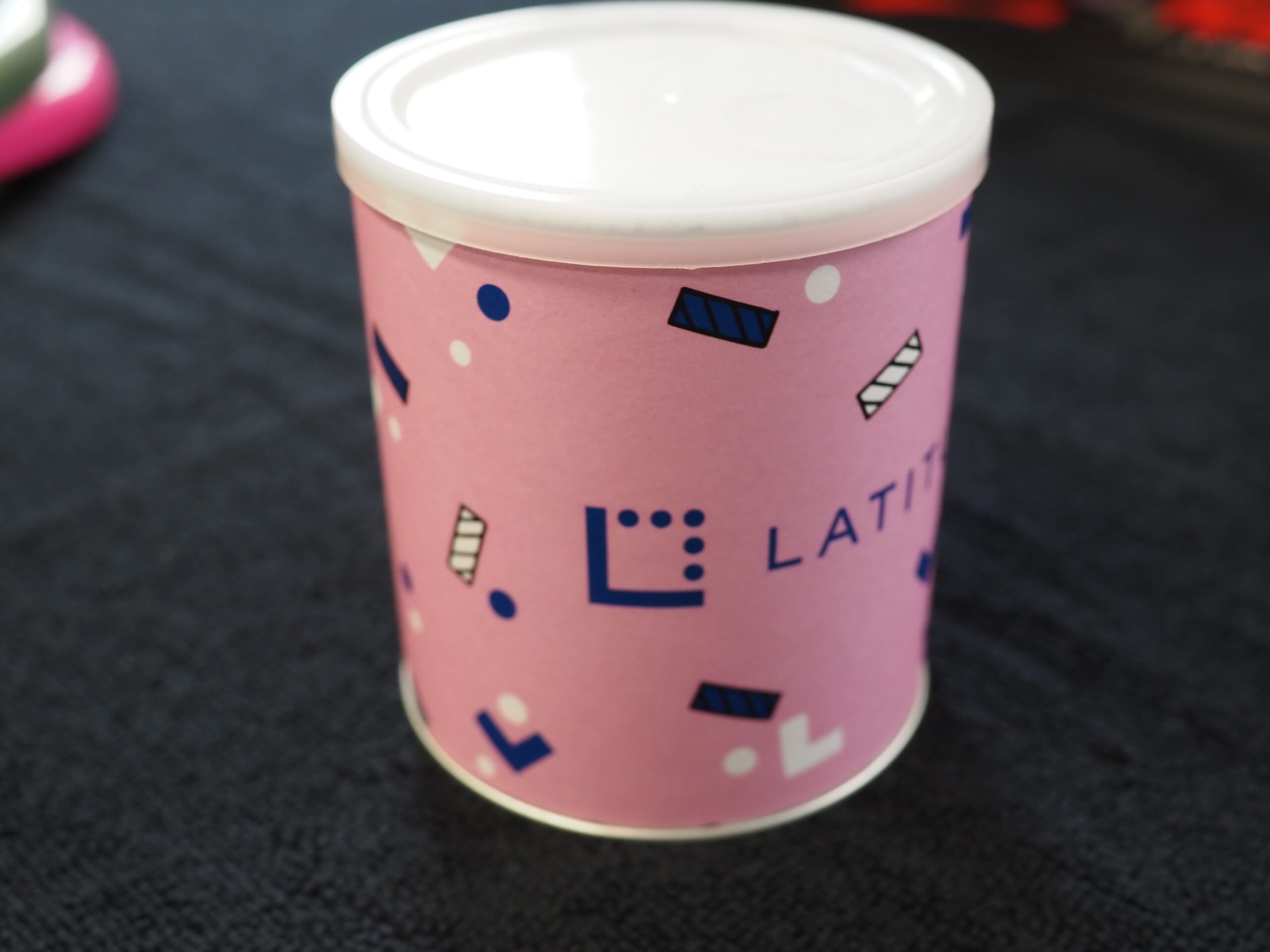 A pink cylindrical container with a white lid, featuring geometric patterns and case study text.