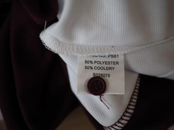 Clothing tag on a polo: 50% polyester, 50% Cooldry, with a button sewn on.