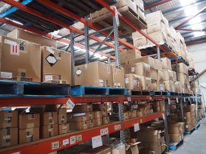 Shelves stacked with cardboard boxes of Promotional products in a warehouse storage area.