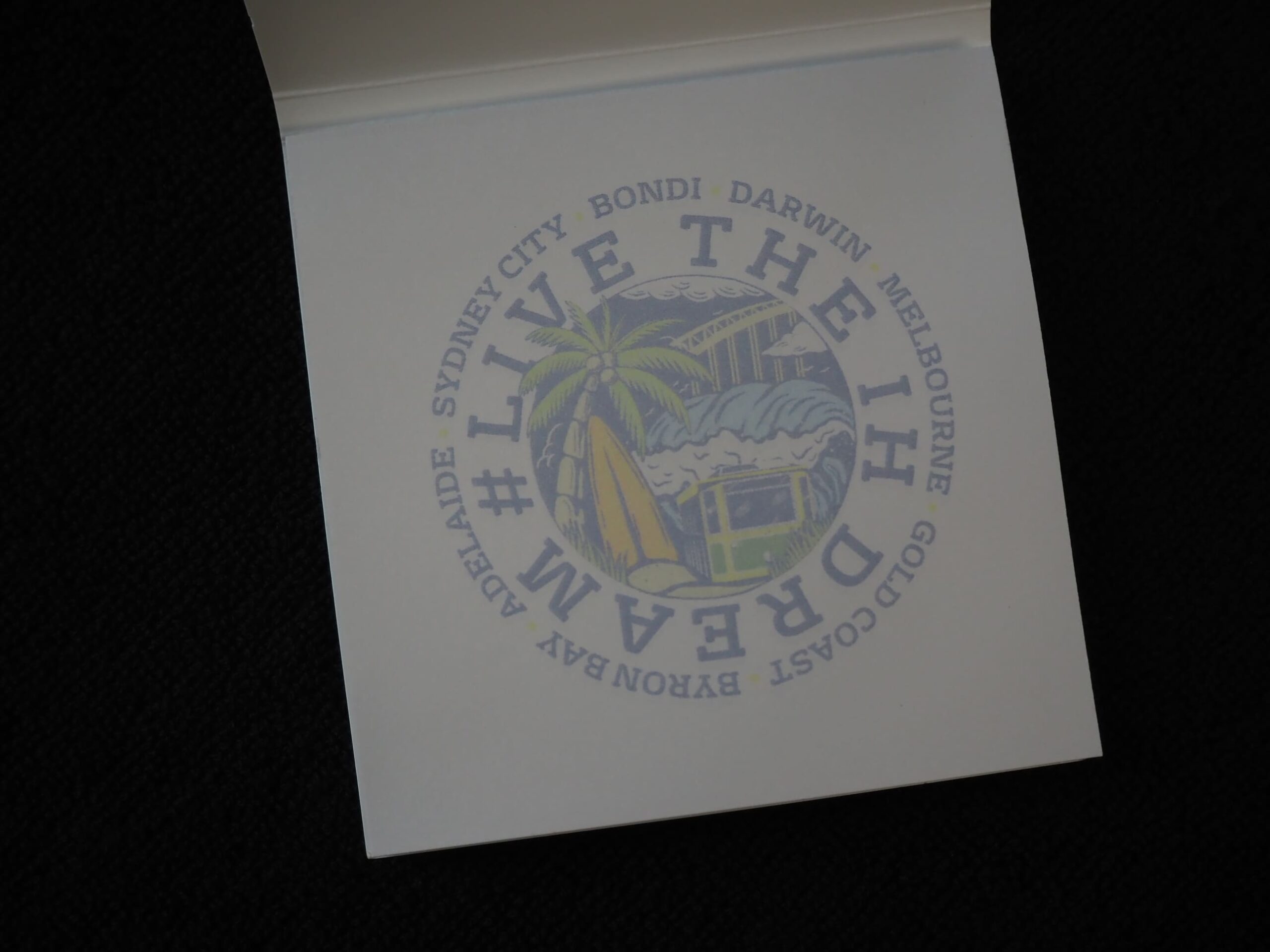 Circular stamp with LIVE THE DREAM, Australian cities, and International House beach scene.