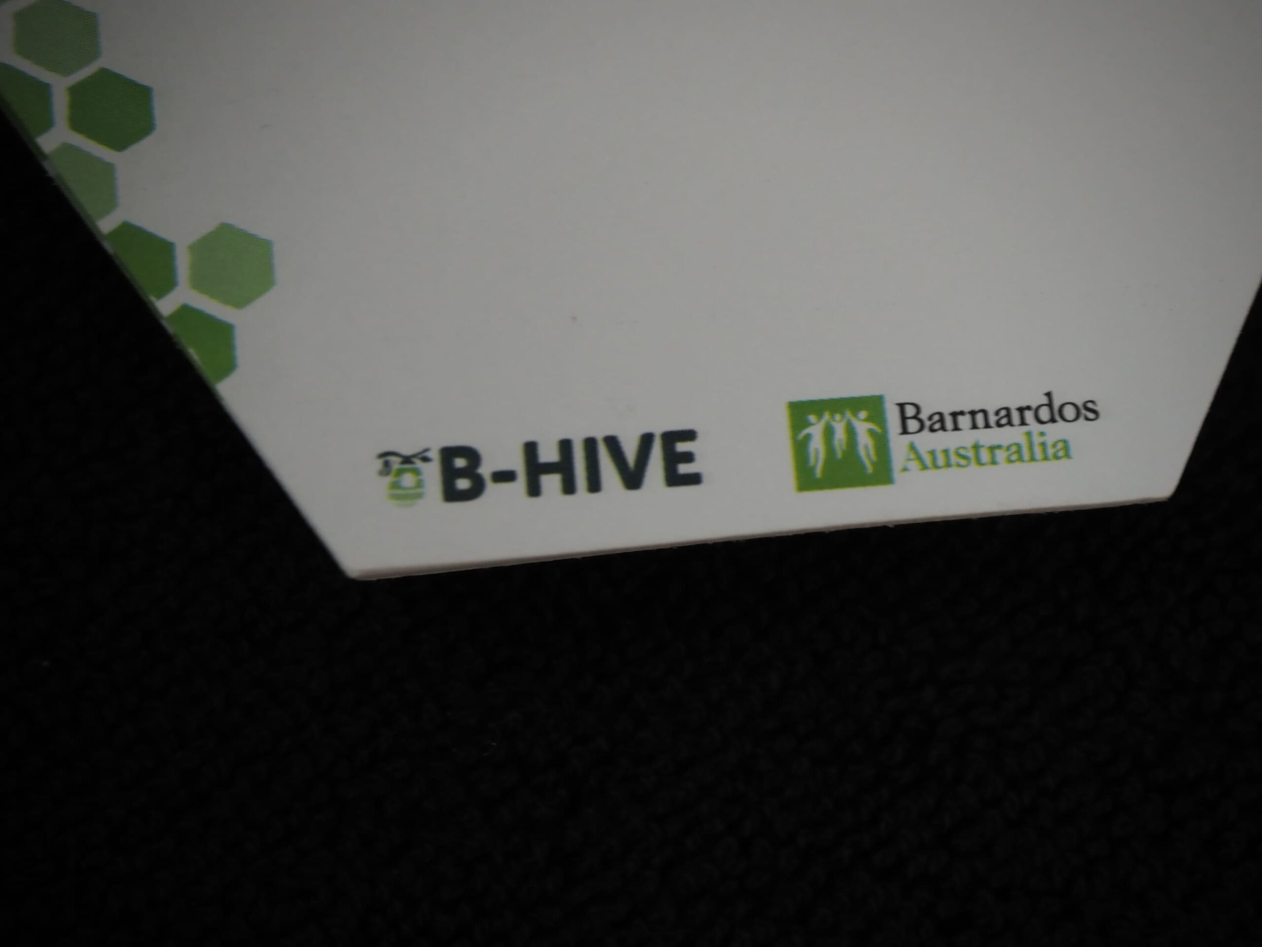 Corner of a paper with B-HIVE and Barnardos Australia child protection logos on a dark surface.