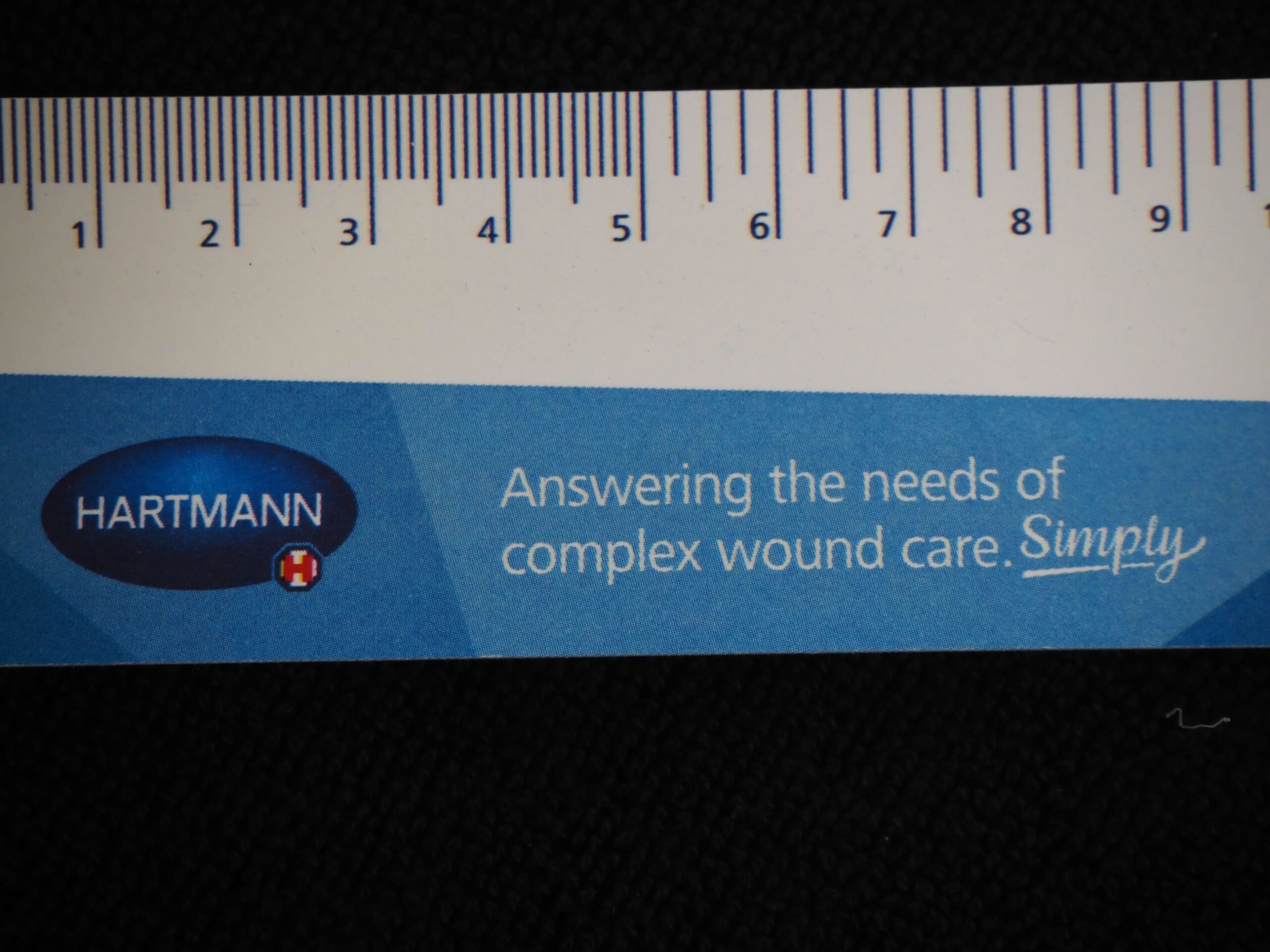 Close-up of a HARTMANN ruler with the slogan, Answering the needs of complex wound care. Simply.