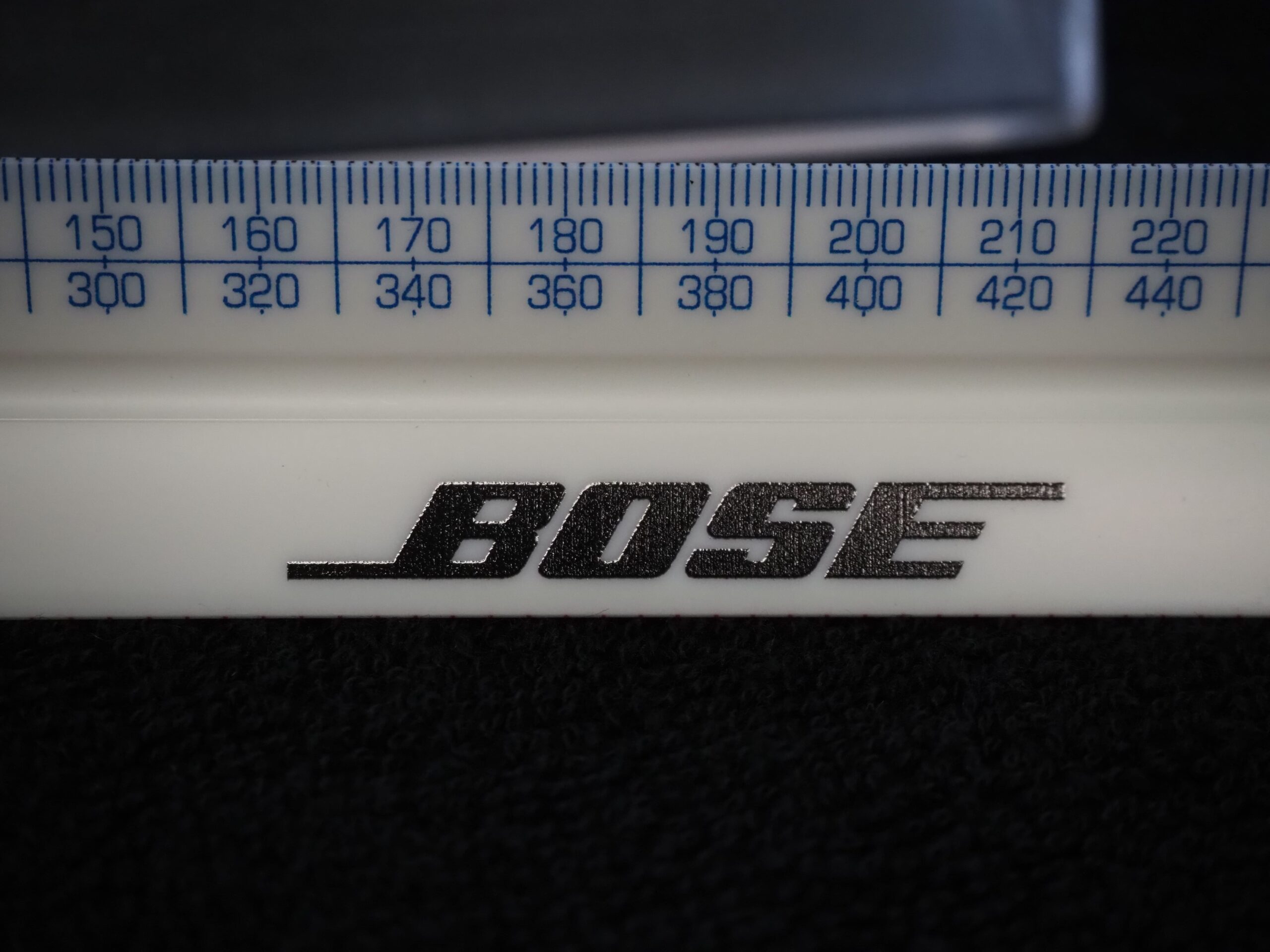 Close-up of a ruler with blue markings and the black Bose logo on a white background.