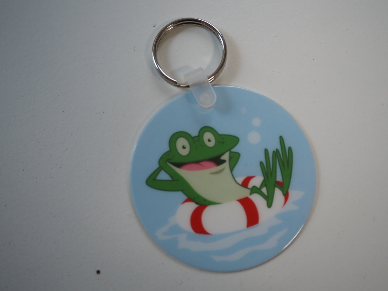 Round keychain with a cartoon frog lounging in water, perfect for Carlile Swimming fans.