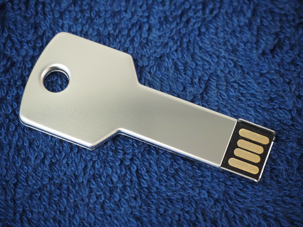 A key-shaped USB flash drive by Era Polymers on a textured dark blue fabric background.