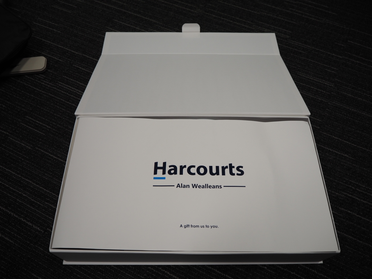 A white gift box with Harcourts branding and Alan Wealleans printed inside.