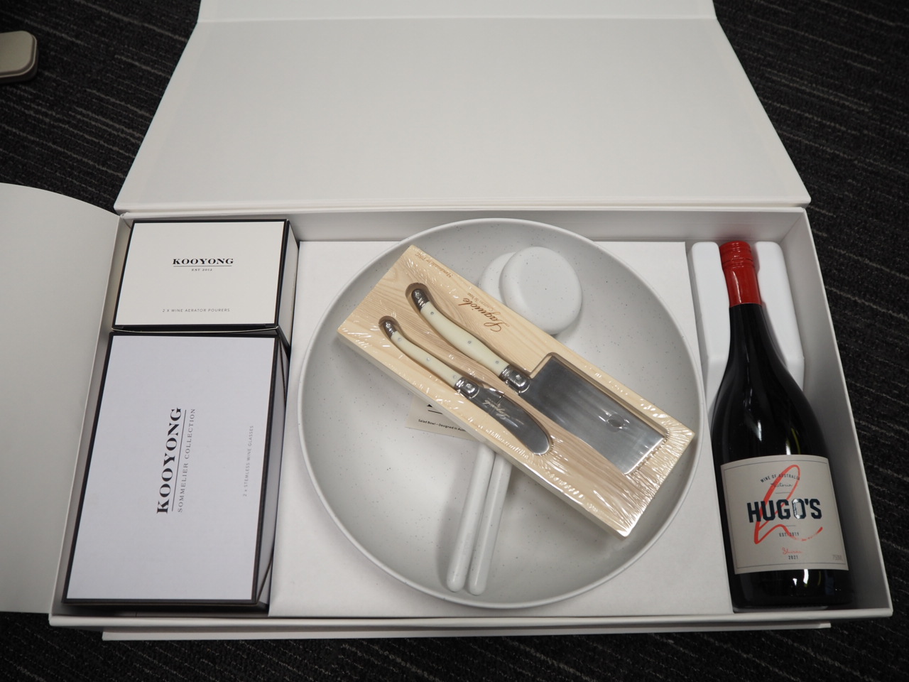 Gift box with wine, cheese knives, a plate, and Alan Wealleans Harcourts branded items displayed.