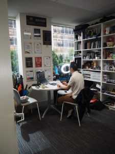 Man working at a desk in a small office with APPA award plaques and shelves of books.