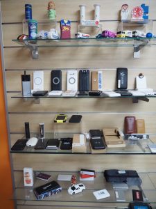 A display of assorted gadgets, toys, and promotional items on glass shelves against a wood wall.