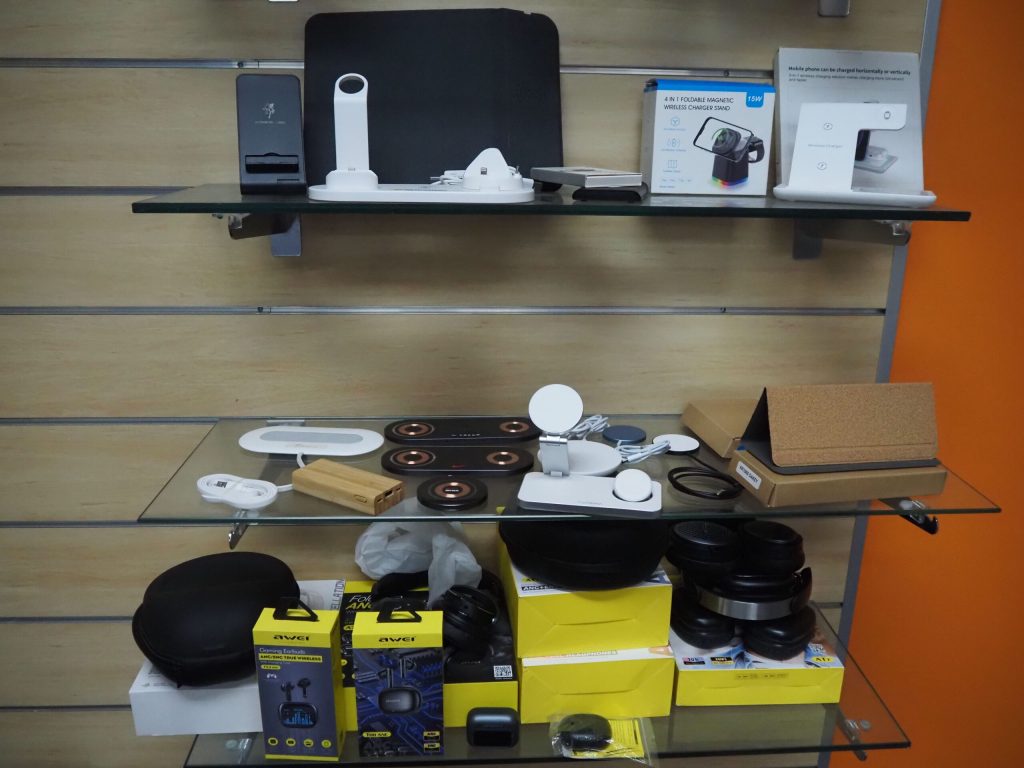 Glass shelves displaying electronic gadgets, chargers, and promotional products in boxes.
